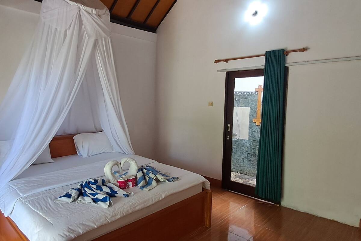 A room with a bed, a curtain, a wooden floor, and a view through a door.