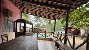 An outdoor patio with a pool, wooden benches, and a covered area with a view of palm trees. - Hotel Fazenda Vale dos Guaribas (Abaíra)