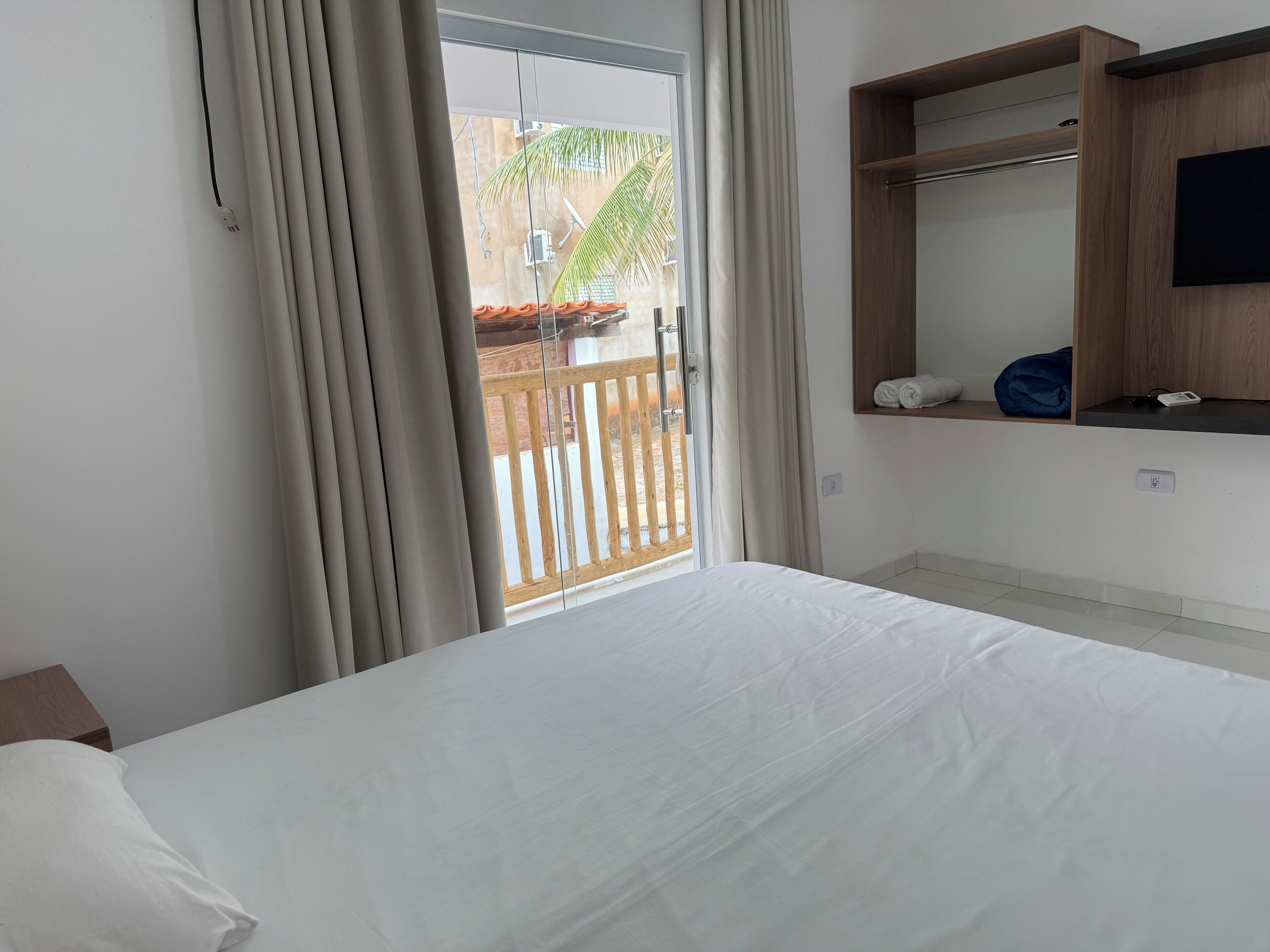 Camera d'albergo con un letto, uno scaffale in legno con asciugamani, una TV e vista del balcone esterno.