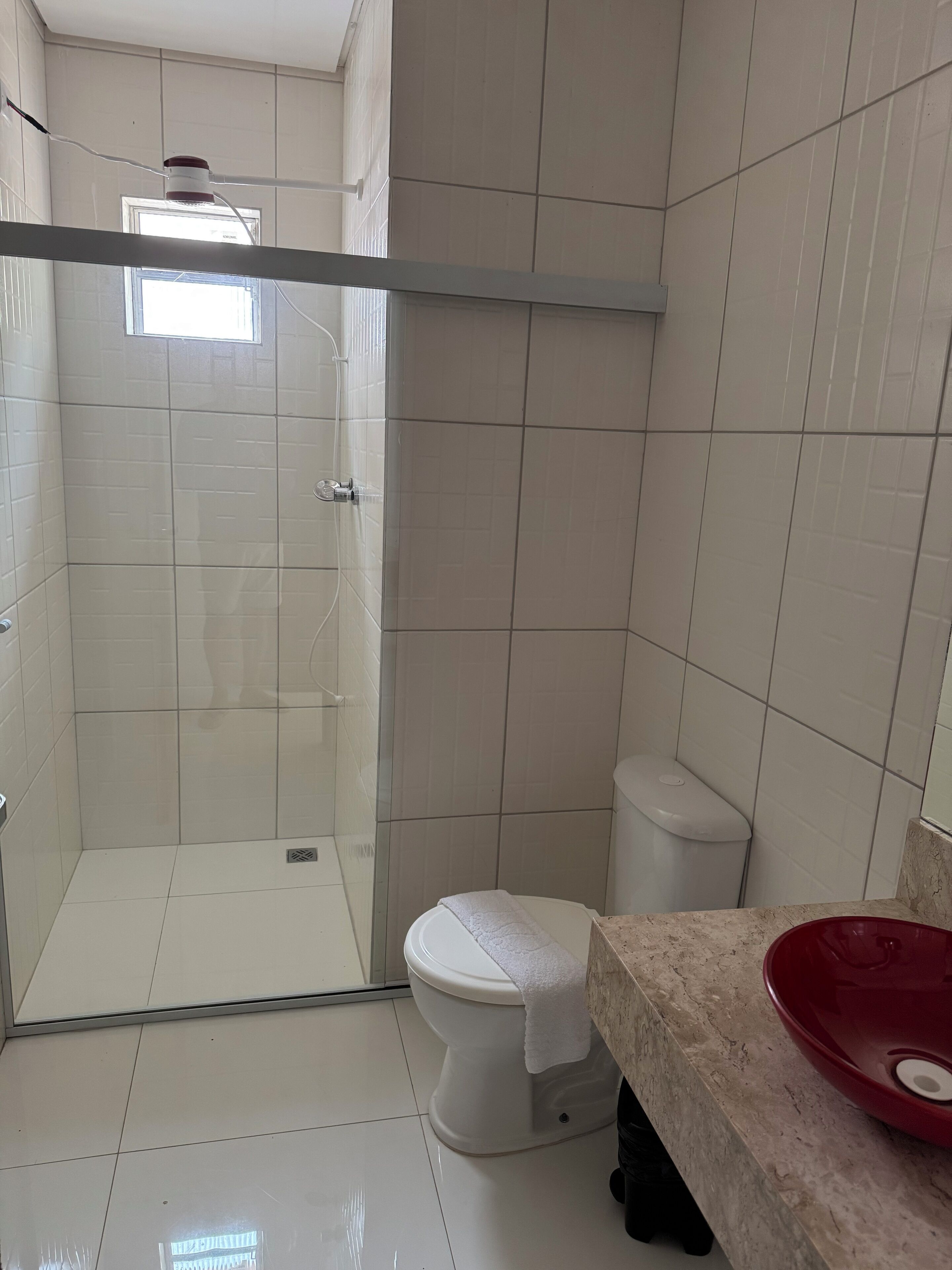 Un baño con cabina de ducha de vidrio, inodoro y lavabo con lavamanos rojo.