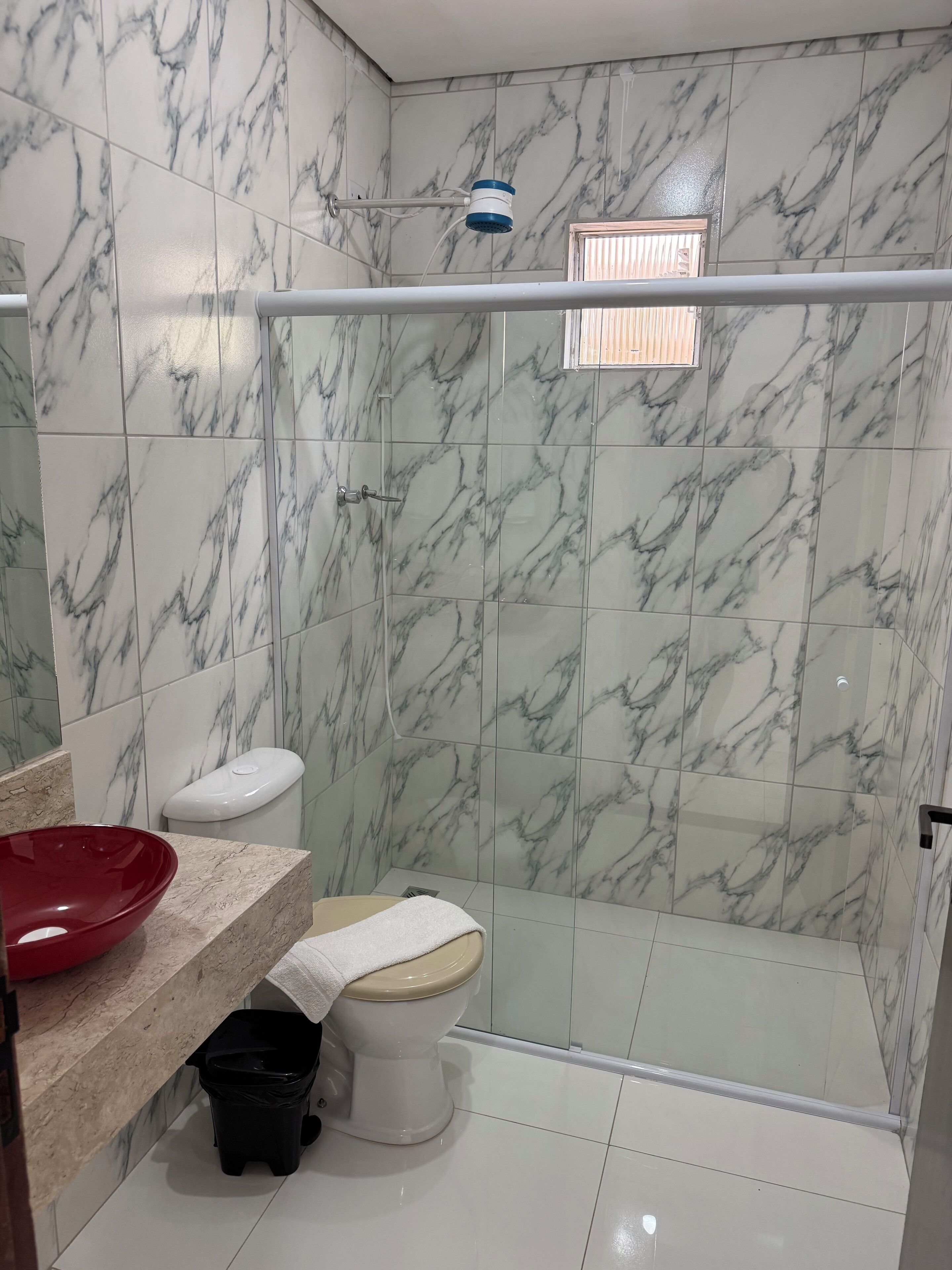 A bathroom with marble tiles, a red basin, a toilet, and a shower area.