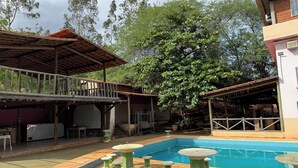 A pool area with a tiled deck, a covered seating area, and a large tree. - Hotel Fazenda Vale dos Guaribas (Abaíra)