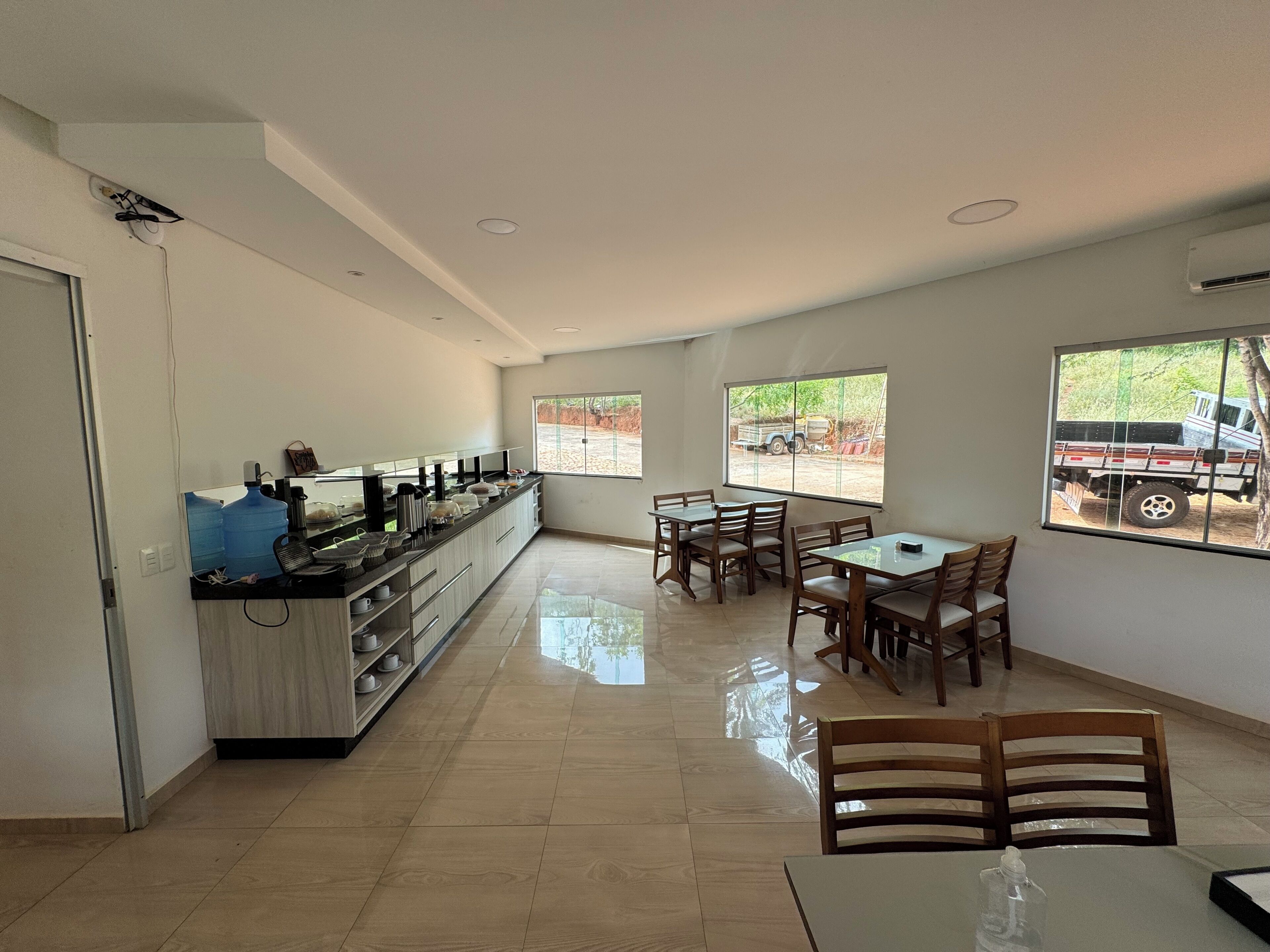 Cozinha espaçosa com bancada comprida, área de jantar com cadeiras de madeira e grandes janelas com vista para o exterior.