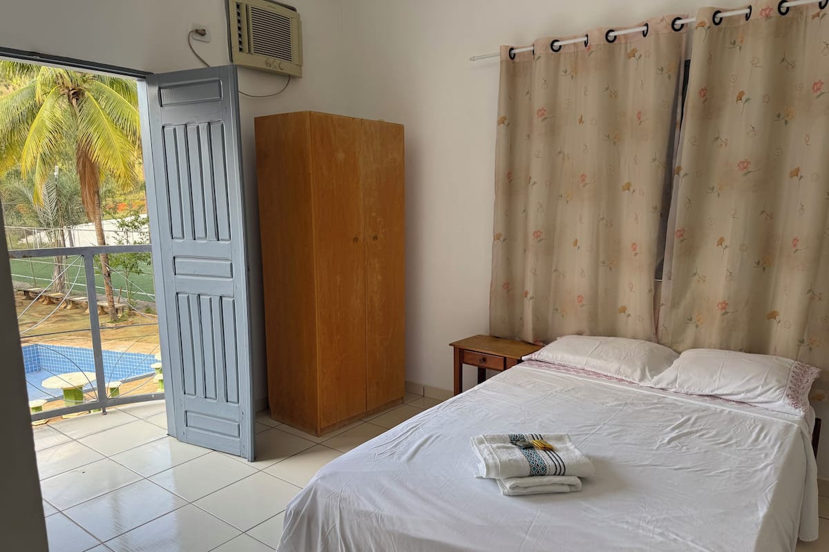 Ein Schlafzimmer mit Bett, einem Holzschrank, einem kleinen Tisch und Blick auf einen Außenpool.