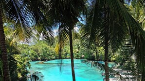 Una playa tropical con agua turquesa cristalina, barcos amarrados en un muelle de madera y exuberante vegetación.