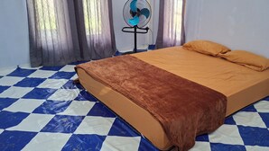 Una habitación con piso a cuadros, una cama con manta marrón, dos almohadas y un ventilador de pie.