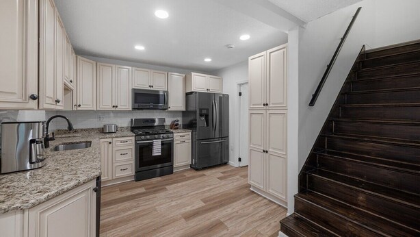 Una cocina moderna con armarios blancos, encimeras de granito, electrodomésticos de acero inoxidable y una escalera de madera oscura.