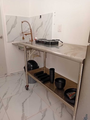 Kitchen area features a gas stove, electric kettle, and bowls on a stainless steel countertop with a marble backsplash.