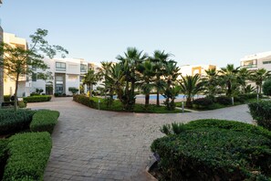Un sendero conduce a una zona de piscina rodeada de edificios modernos y abundante vegetación.