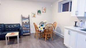 Una sala de estar con sofá, una mesa de centro, una mesa de comedor con sillas, una estantería y una cocina con armarios y una ventana.