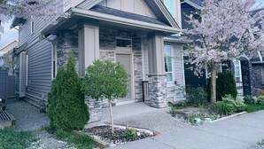 Una casa moderna de dos pisos con fachada de piedra, un porche delantero y un jardín cuidado.