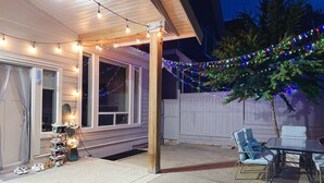 Un patio cubierto con luces colgantes, una terraza de madera y mobiliario exterior.