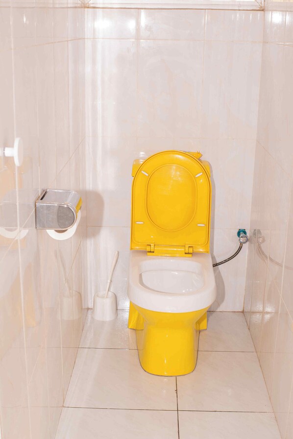 Een badkamer met een geel toilet, een witte spoelknop en een toiletrolhouder bevestigd aan de muur.