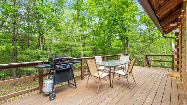 A wooden deck with a grill and table, surrounded by trees.