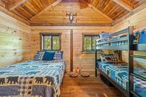 A cabin with a wooden interior, a bunk bed, a fireplace, and a window with a view of trees.