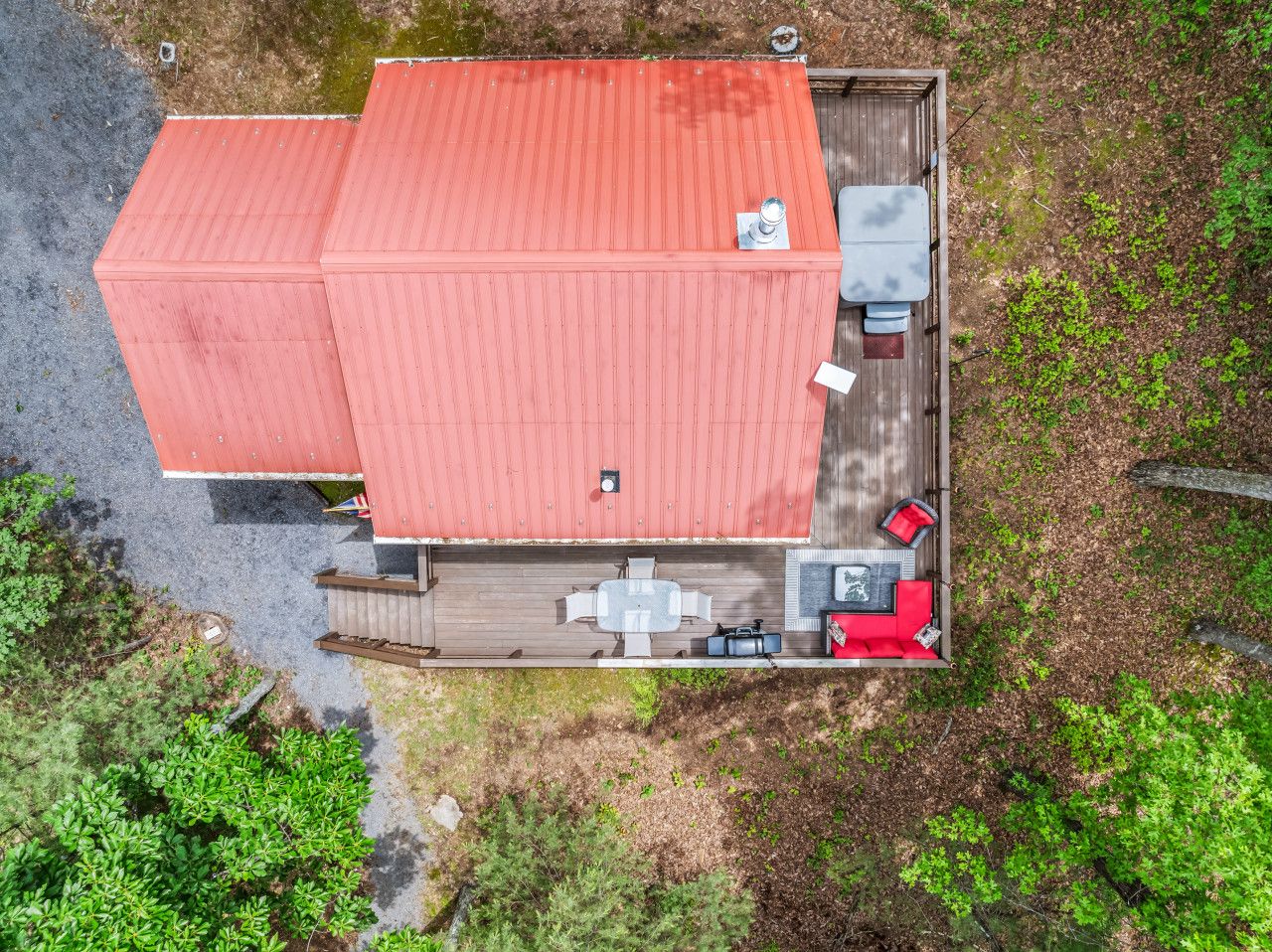 A two-story building with a red roof, a deck with outdoor seating, and a small garden area.