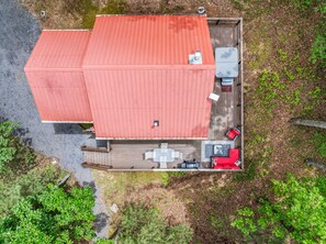 A two-story building with a red roof, a deck with outdoor seating, and a small garden area.