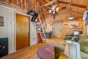 A cozy cabin interior with a wooden staircase, a dining area, and a living room with a sofa and lamp.