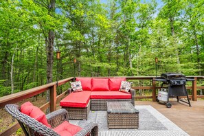 A deck with a red sofa, wicker chairs, and a grill.
