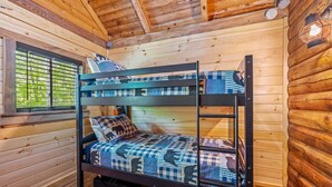 A bunk bed in a wooden cabin room with a window and a ladder.