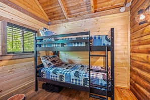 Una cama litera en una habitación tipo cabaña de madera, con ventana y escalera.