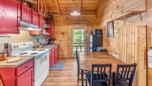 A cabin-style kitchen with wooden walls, a white stove, red cabinets, and a dining table with chairs.