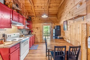 Una cocina tipo cabaña con paredes de madera, una estufa blanca, armarios rojos y una mesa de comedor con sillas.