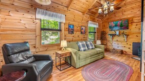 A wooden cabin interior with a leather sofa, a green couch, a wooden coffee table, and a fireplace.