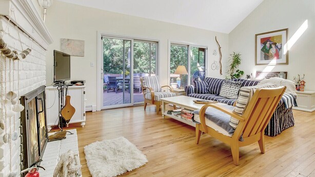 A spacious living room with a fireplace, a sofa set, a wooden coffee table, and a view through large sliding glass doors to an outdoor area.