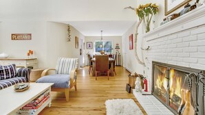 A cozy living room with a fireplace, a dining area, and a playland sign on the wall.