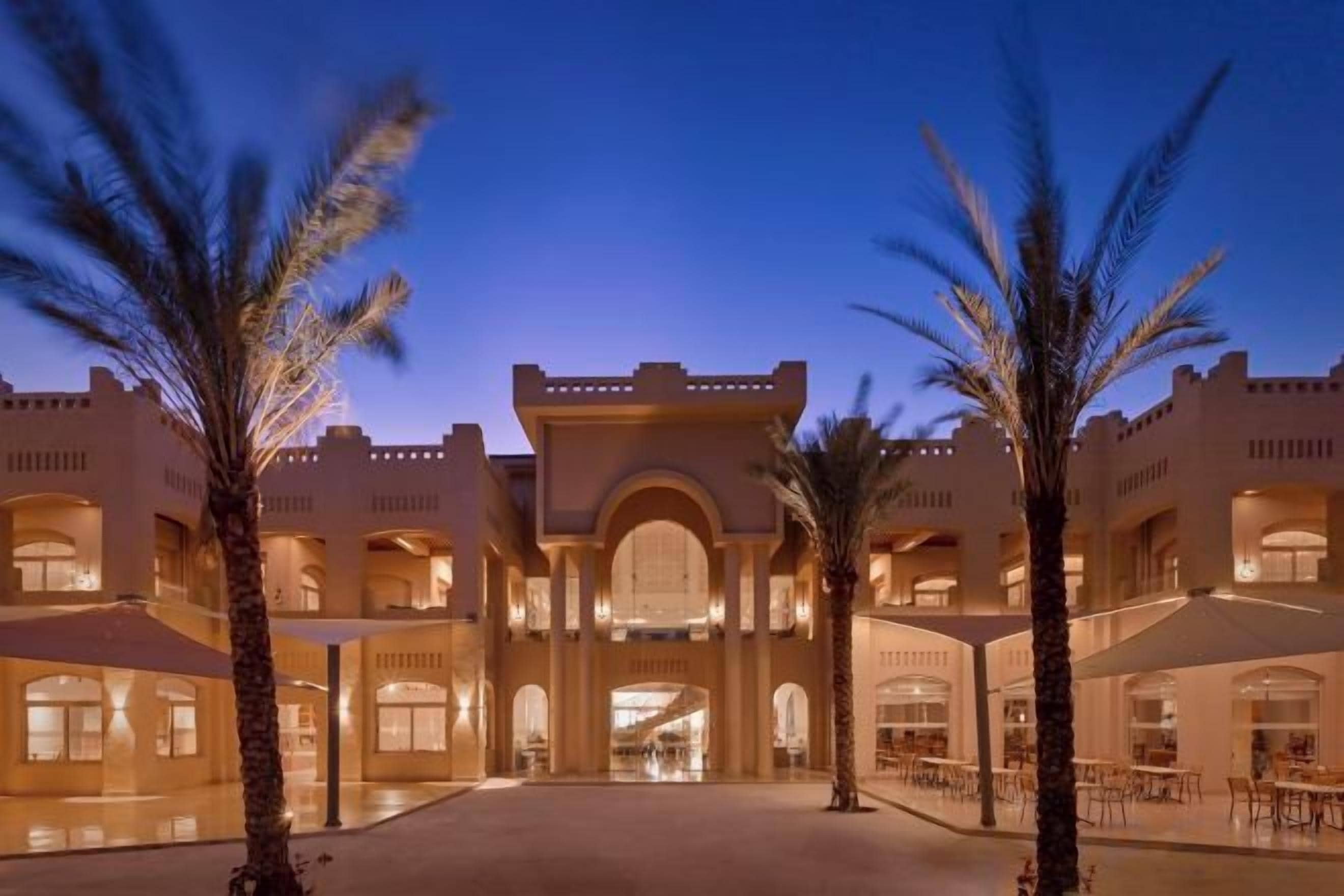 A hotel courtyard with palm trees, a central archway, and multiple levels of balconies.