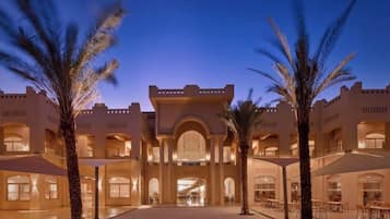 A hotel courtyard with palm trees, a central archway, and multiple levels of balconies.