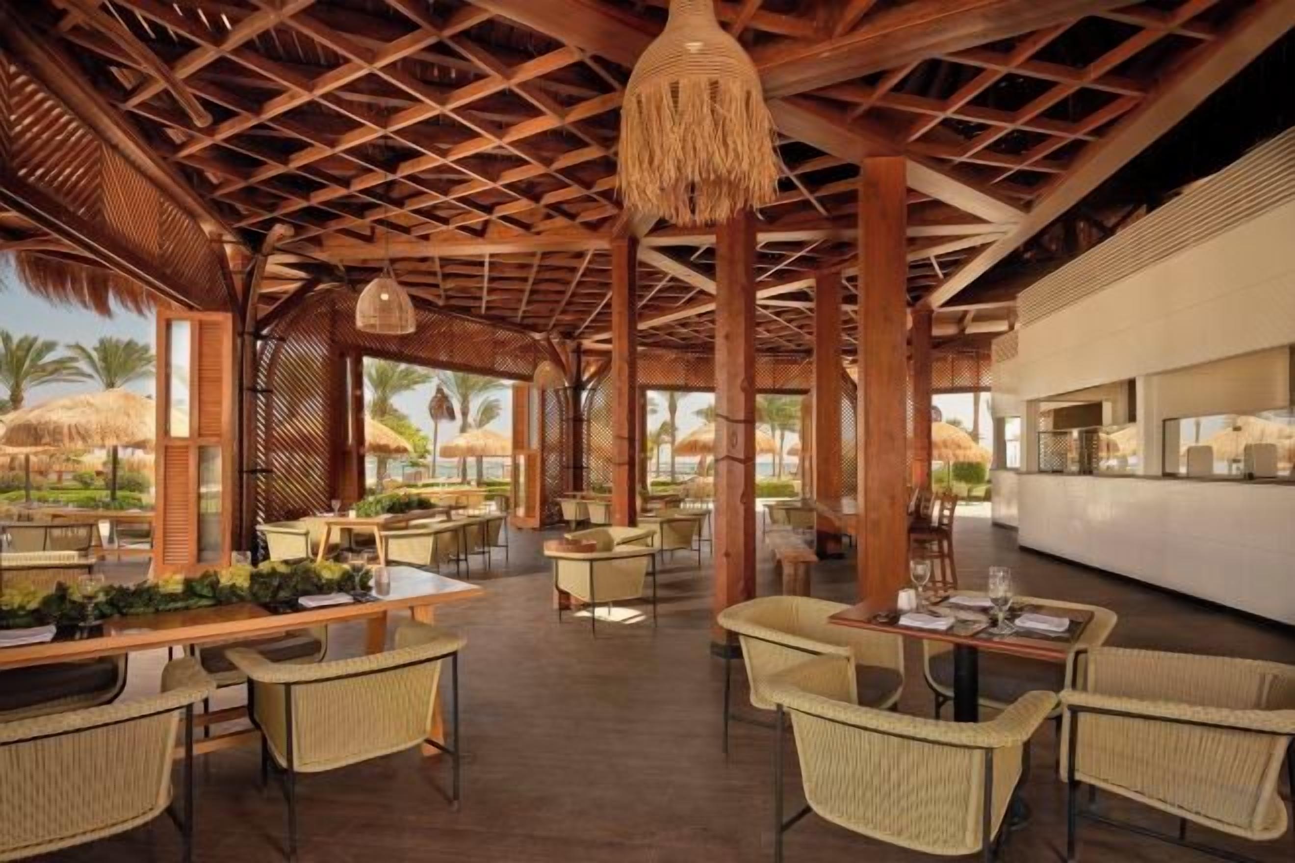 A covered outdoor dining area with wicker furniture and a thatched ceiling.