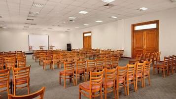 A conference room with rows of wooden chairs, a projector screen, and a large wooden door.