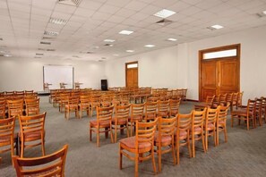 A conference room with rows of wooden chairs, a projector screen, and a large wooden door.