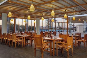 Un restaurant avec des tables et des chaises en bois, des lampes suspendues et de grandes fenêtres.