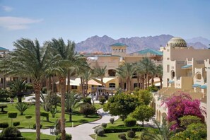 A hotel courtyard with palm trees, a pathway, and mountain views.