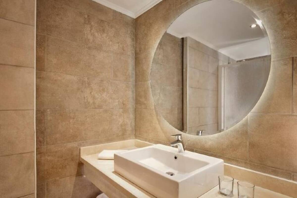 Un baño moderno con un espejo ovalado grande, un lavabo rectangular y un mueble de tocador con una toalla.