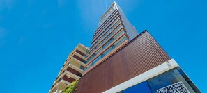 Ένα σύγχρονο πολυώροφο κτίριο με εντυπωσιακή κάθετη αρχιτεκτονική, που διαθέτει πολλά μπαλκόνια και συνδυάζει στοιχεία πρόσοψης από γυαλί και ξύλο.