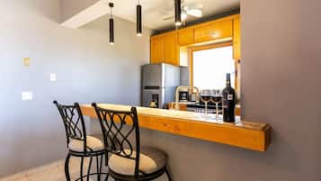 A kitchen with a bar area, two bar stools, a ceiling fan, and a refrigerator.