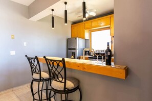Une cuisine avec un coin bar, deux tabourets de bar, un ventilateur de plafond et un réfrigérateur.