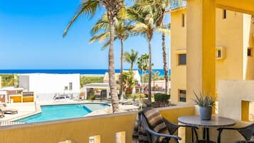 A poolside area with a view of the ocean, palm trees, and a yellow building.