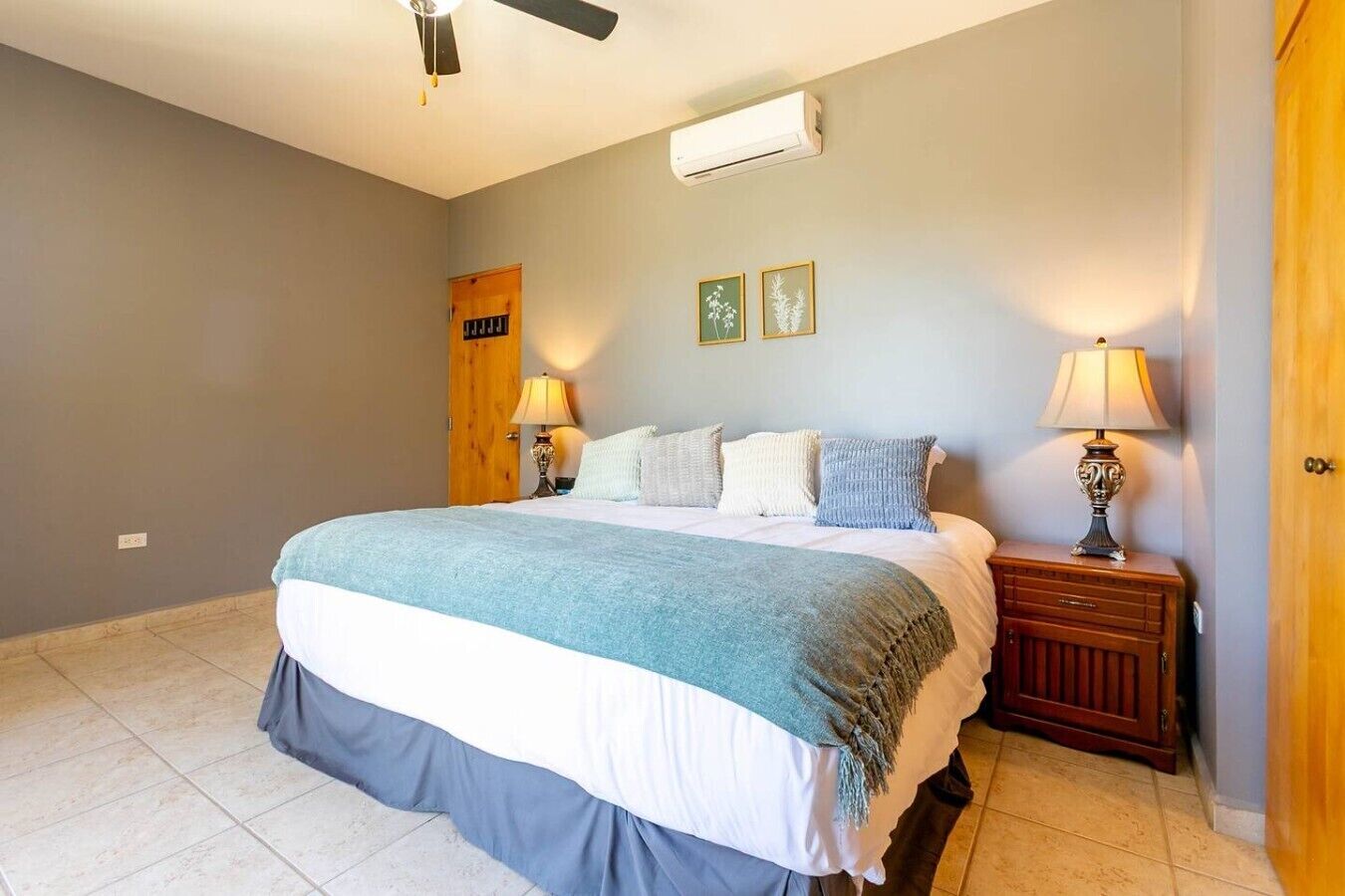 A bedroom with a bed, bedside lamps, a wooden door, and a wall-mounted air conditioner.