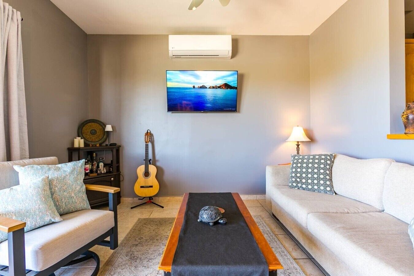 Una sala de estar con un sofá, una mesa de centro, una guitarra y un televisor montado en la pared.