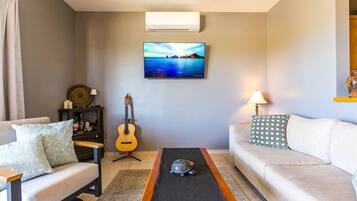 Una sala de estar con un sofá, una mesa de centro, una guitarra y un televisor montado en la pared.