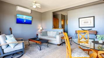 A living room with a sofa, a coffee table, a TV mounted on the wall, and a ceiling fan.