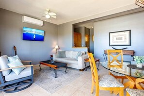 Un salon comprenant un canapé, une table basse, un téléviseur fixé au mur et un ventilateur de plafond.