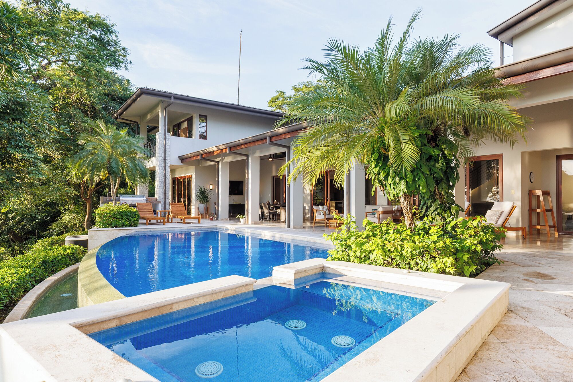 Una casa moderna amb piscina, mobiliari exterior i vegetació exuberanta.