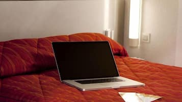 Ein Laptop auf einem Bett mit roter Bettdecke und Kissen.