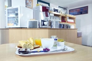 A breakfast tray with toast, orange juice, and a bowl of yogurt on a table in a hotel room. - Premiere Classe Poitiers Futuroscope - Chasseneuil (Chasseneuil-du-Poitou)